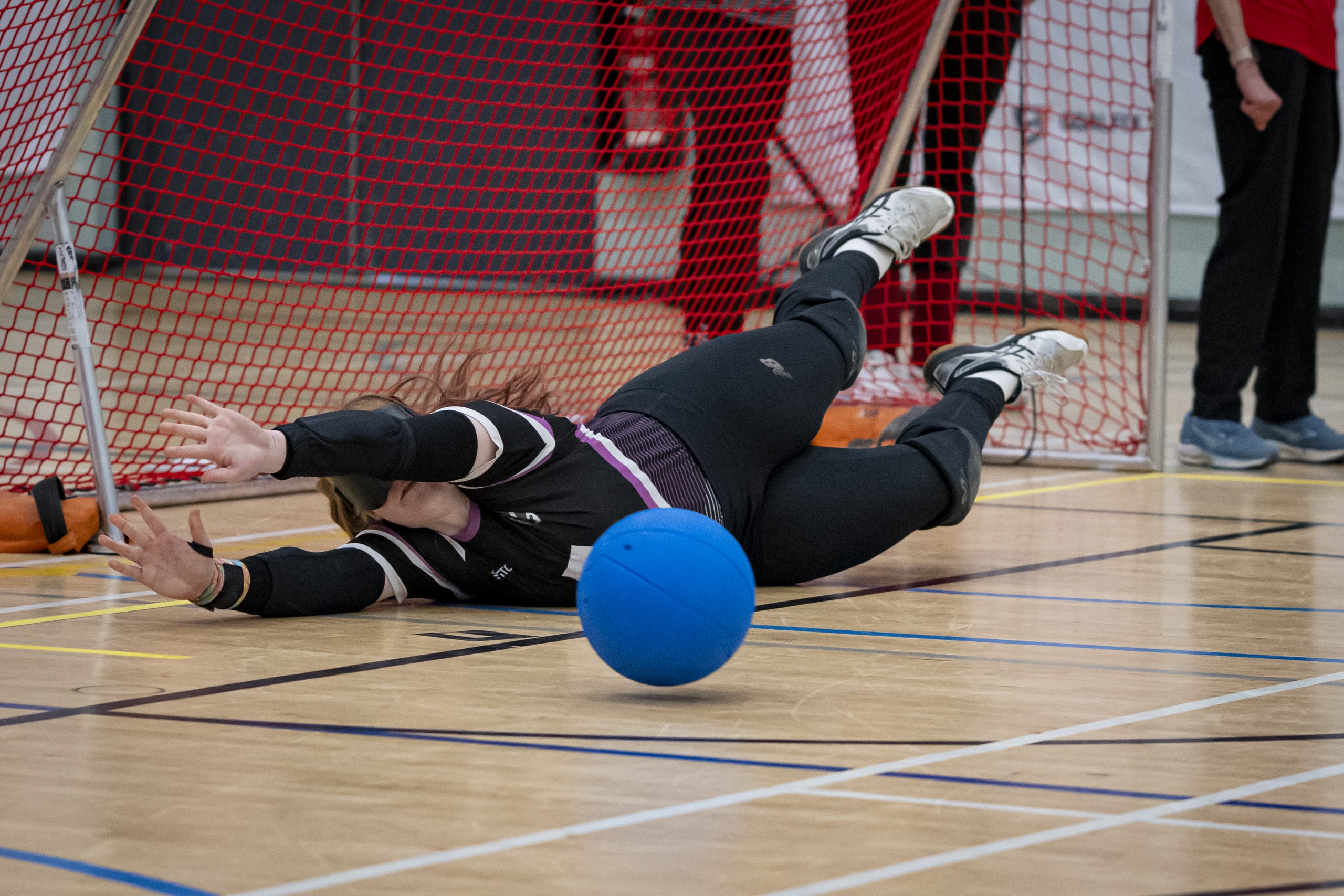 A female goalball player dives across the court reaching for the ball