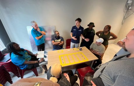 Alex Bunney standing next to a table with a goalball court marked out on it explaining the rule to a group