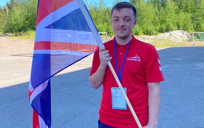 Alex Cockerham at the European Para Youth Games, holding a large Union Jack flag ready for the Opening Ceremony.