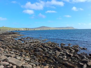 A view across a rocky shoreline, across the sea, to another island.